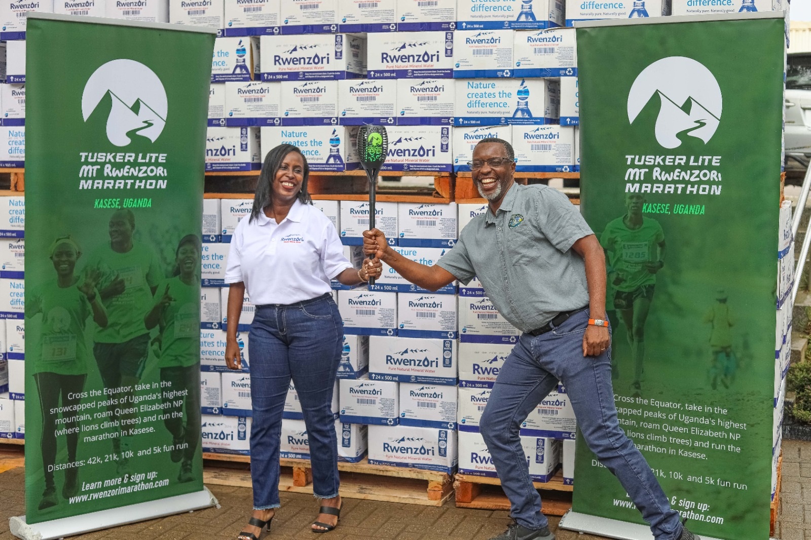 Pearl Nimusiima, the Public Affairs and Communications Manager of CCBU shakes hands with Amos Wekesa, the Tusker Lite Mt.Rwenzori Marathon  Team Leader  as she hands over a dummy cheque worth UGX 173m and boxes of Rwenzori  Pure Natural Mineral Water ahead of the Marathon